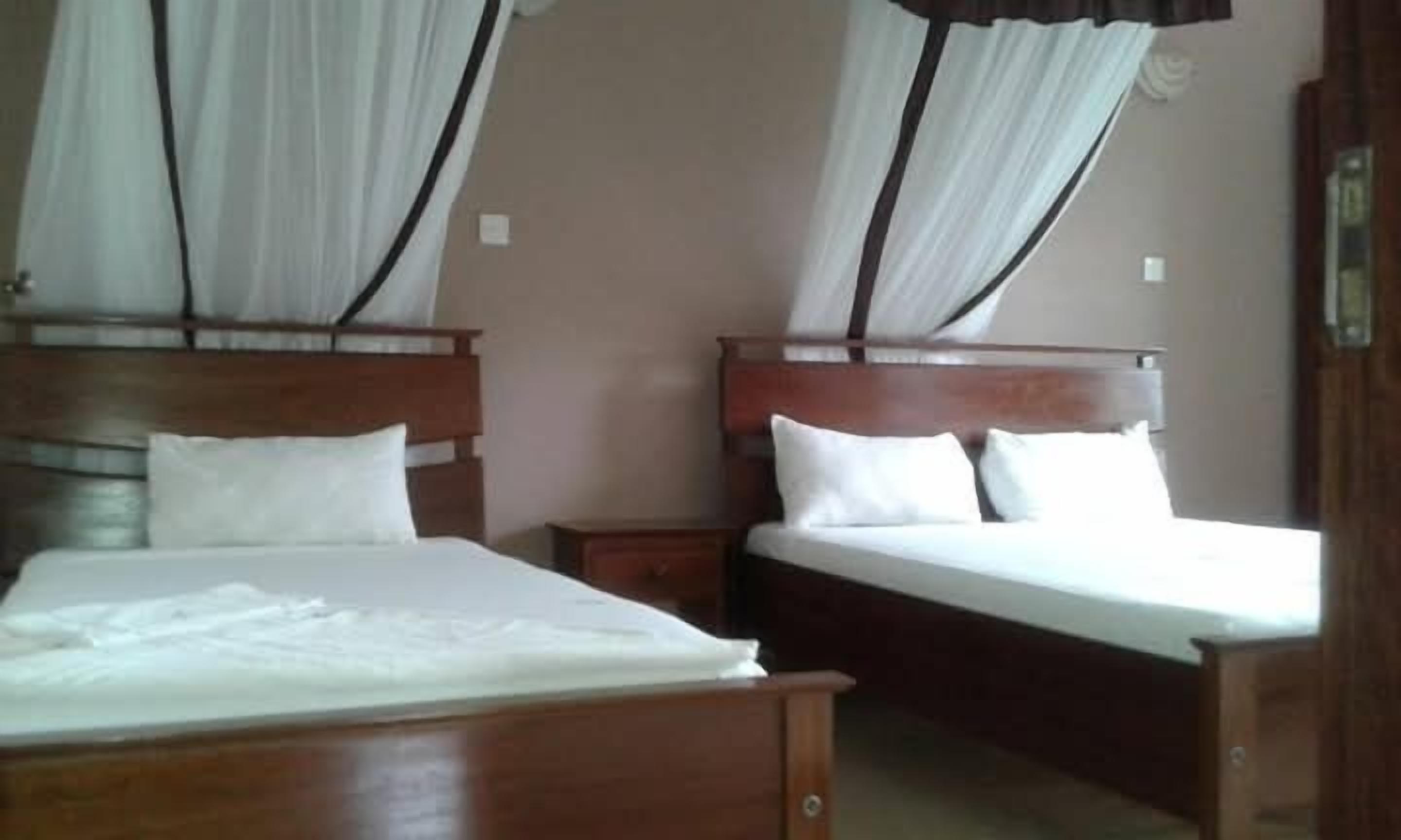 A hotel room with two wooden beds, each with white bedding and curtains.