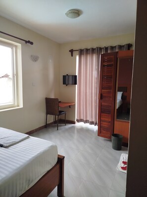 Un dormitorio con cama, escritorio, silla, televisor y puerta de baño.