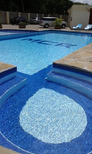 A swimming pool with clear blue water, steps leading into the pool, and a few lounge chairs in the background. - MTWAPA COUNTRY RESORT (Mtwapa)