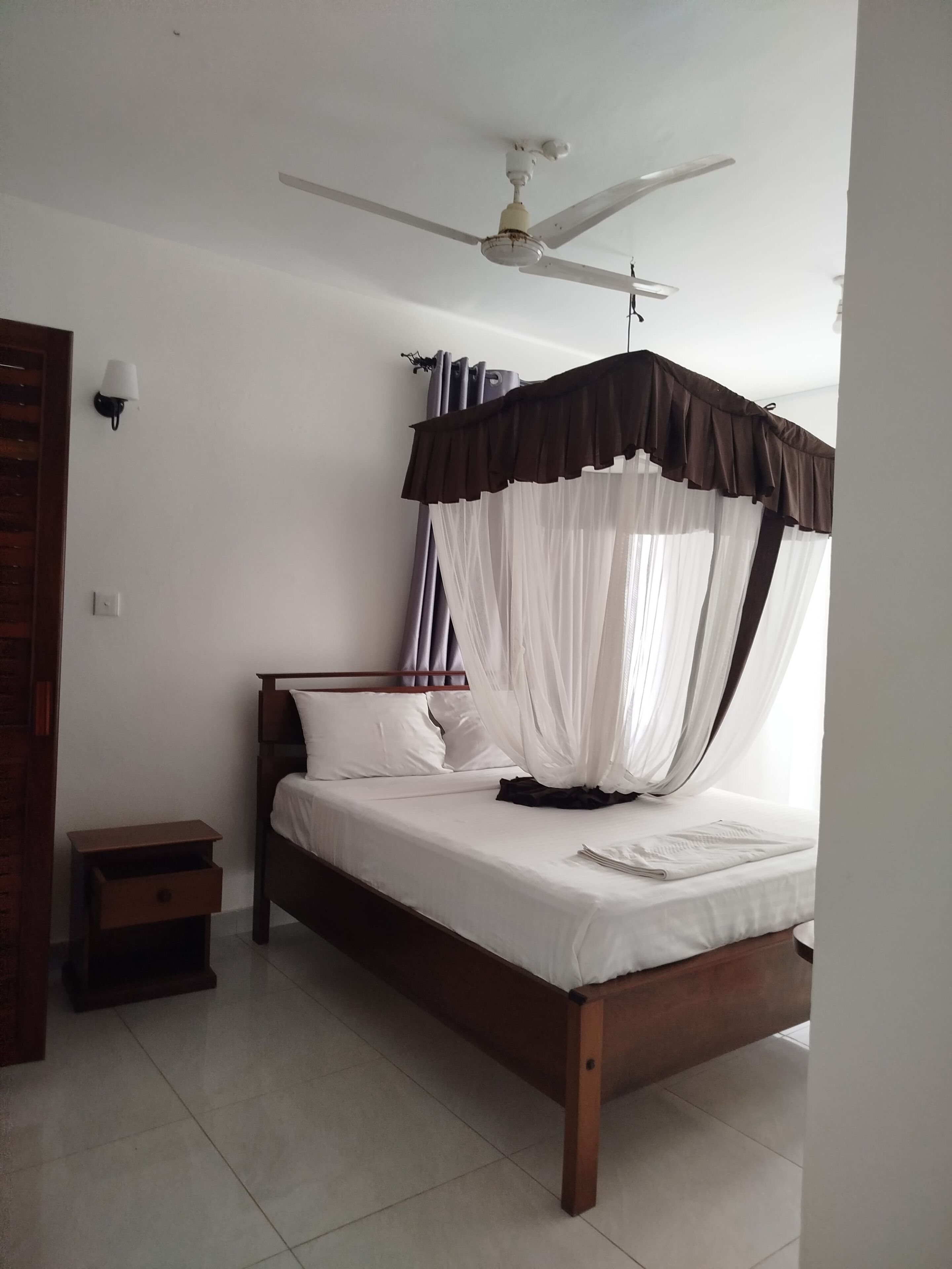 A bedroom with a bed, a nightstand, a ceiling fan, and a wall-mounted lamp.