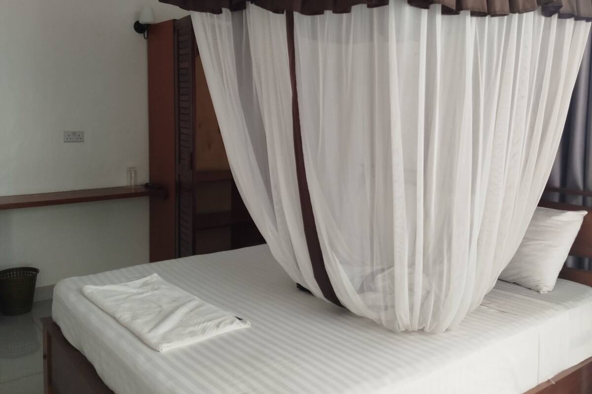 Un dormitorio con una cama, cortinas blancas, un ventilador de techo y un cabecero de madera.