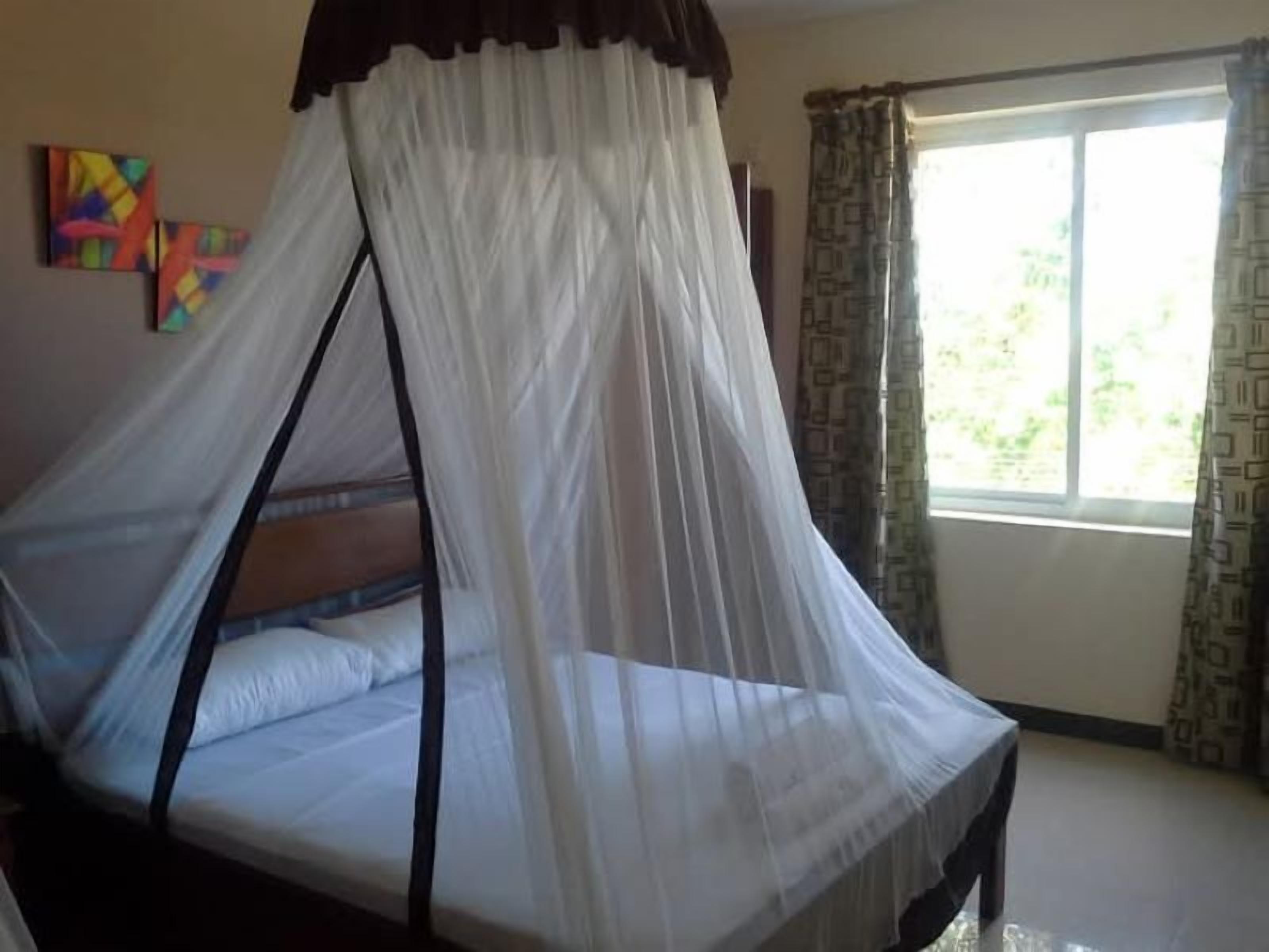 A room with a bed under a canopy, a window with curtains, and a painting on the wall.