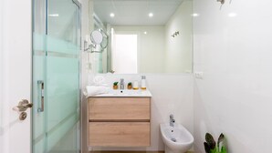Une salle de bain moderne avec une douche à l’italienne en verre, un meuble-lavabo en bois, un lavabo blanc et un bidet.