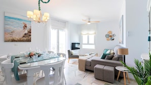 Un salon moderne avec une table à manger en verre, des chaises blanches, un canapé gris et un ventilateur de plafond.
