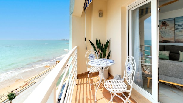 Un balcon avec vue sur la plage, une table avec des chaises et une porte-fenêtre coulissante donnant sur l’espace de vie.