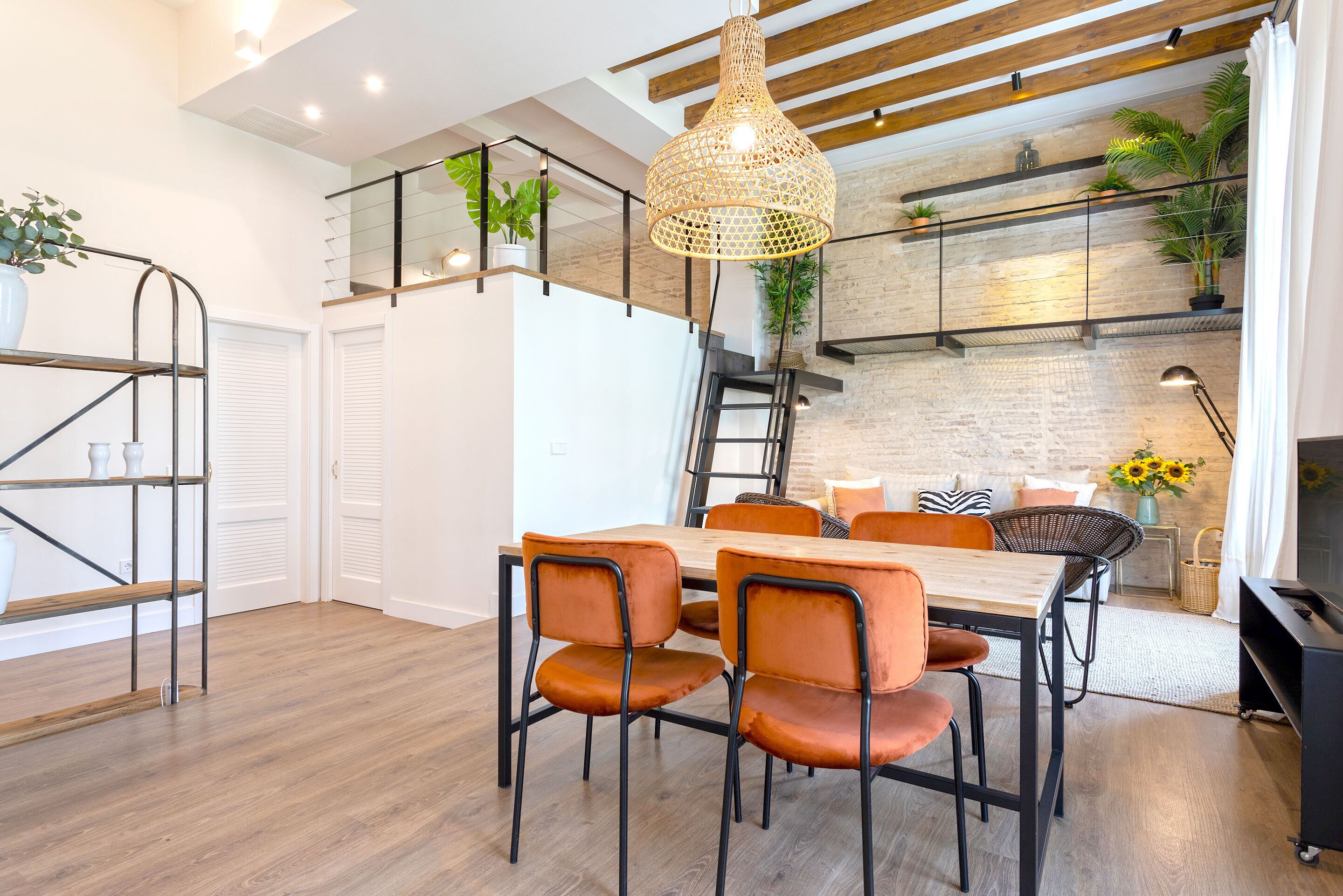Un comedor moderno con una mesa de madera, sillas color naranja y una lámpara colgante.