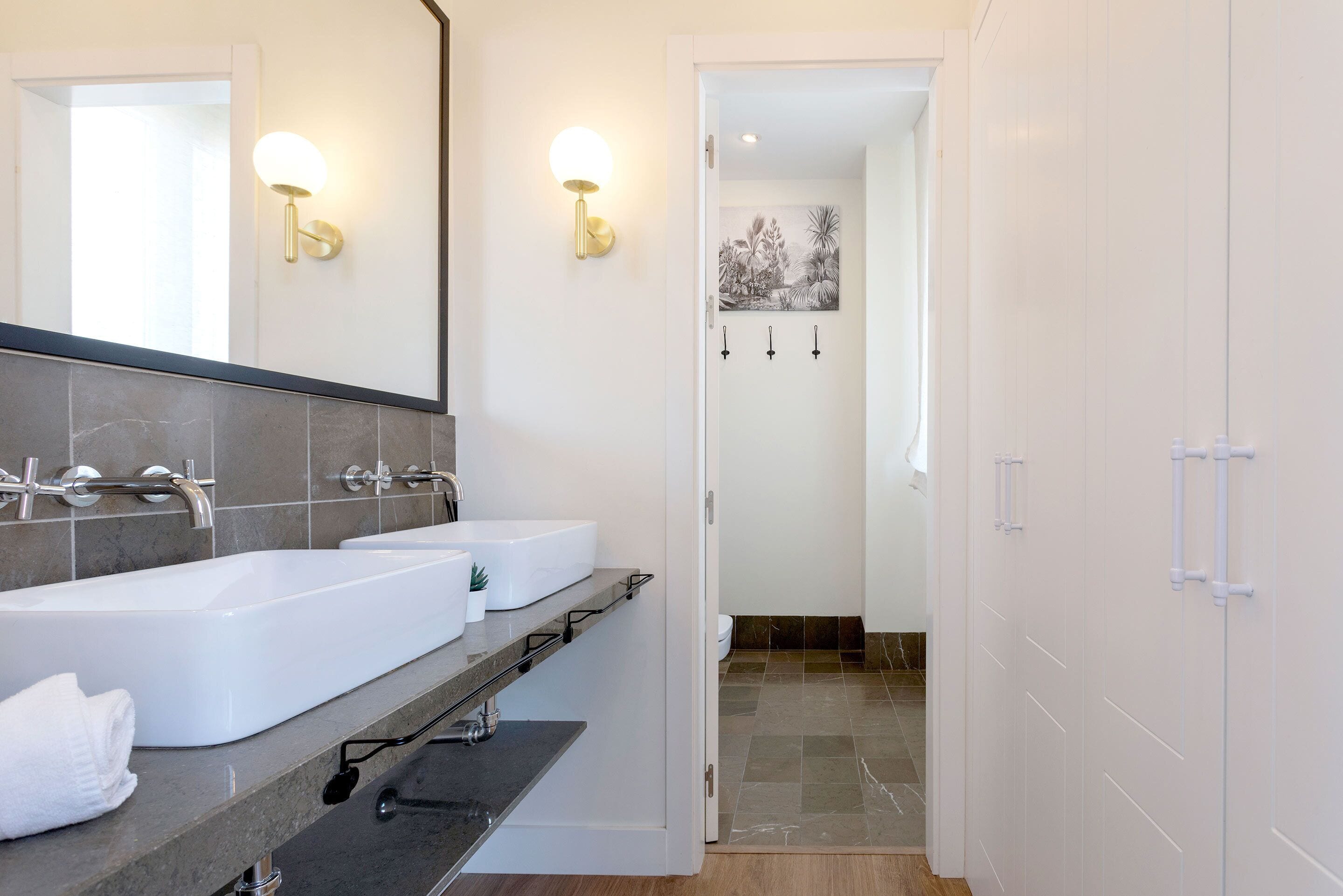 A modern bathroom with two sinks, a large mirror, and wall-mounted light fixtures.