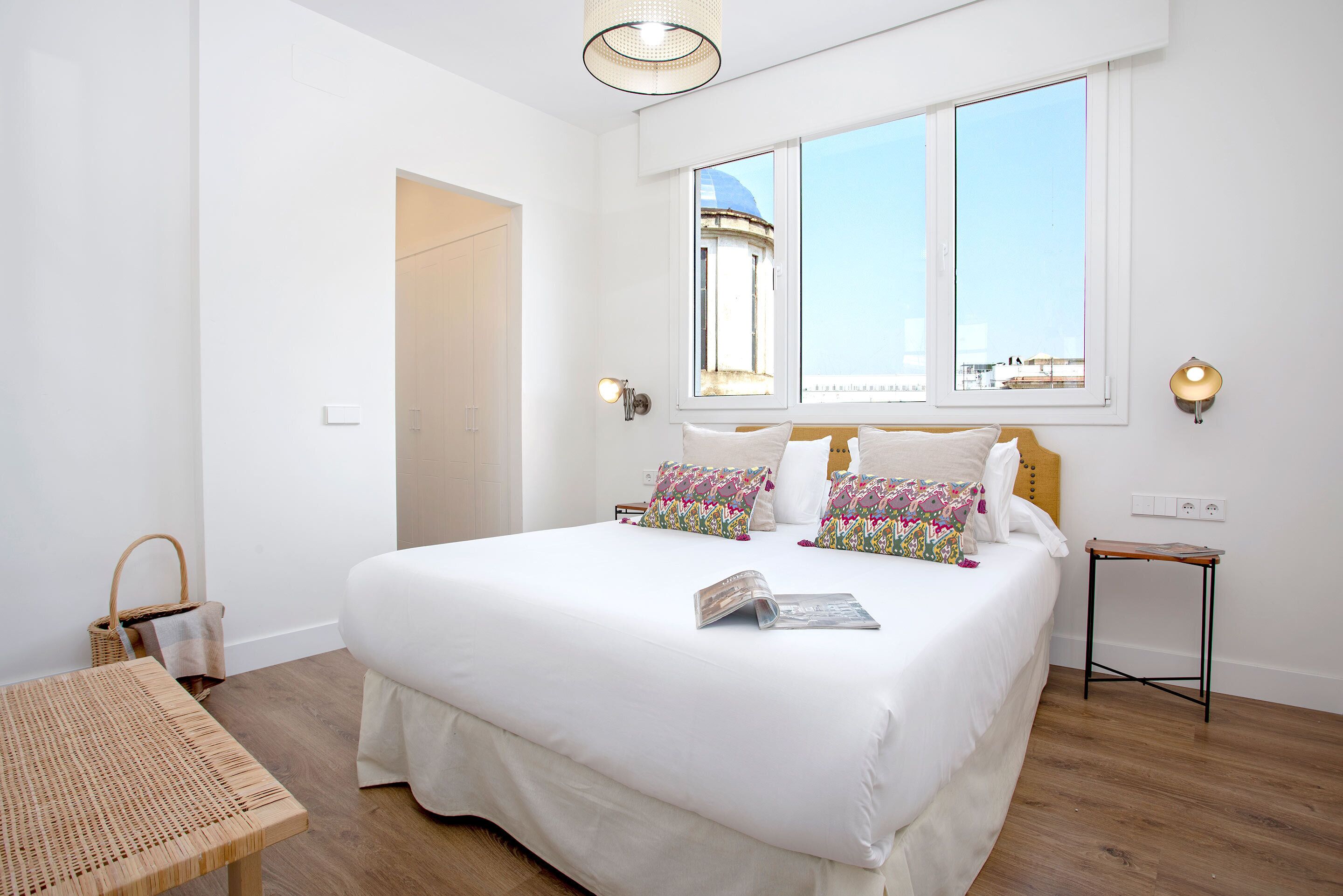 Un dormitorio amplio con una cama grande, una mesa de madera y vistas a un edificio desde la ventana.