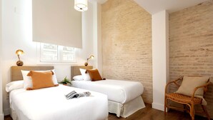 Ein Hotelzimmer mit zwei Betten, Holzboden, Ziegelwand und einem Korbstuhl.