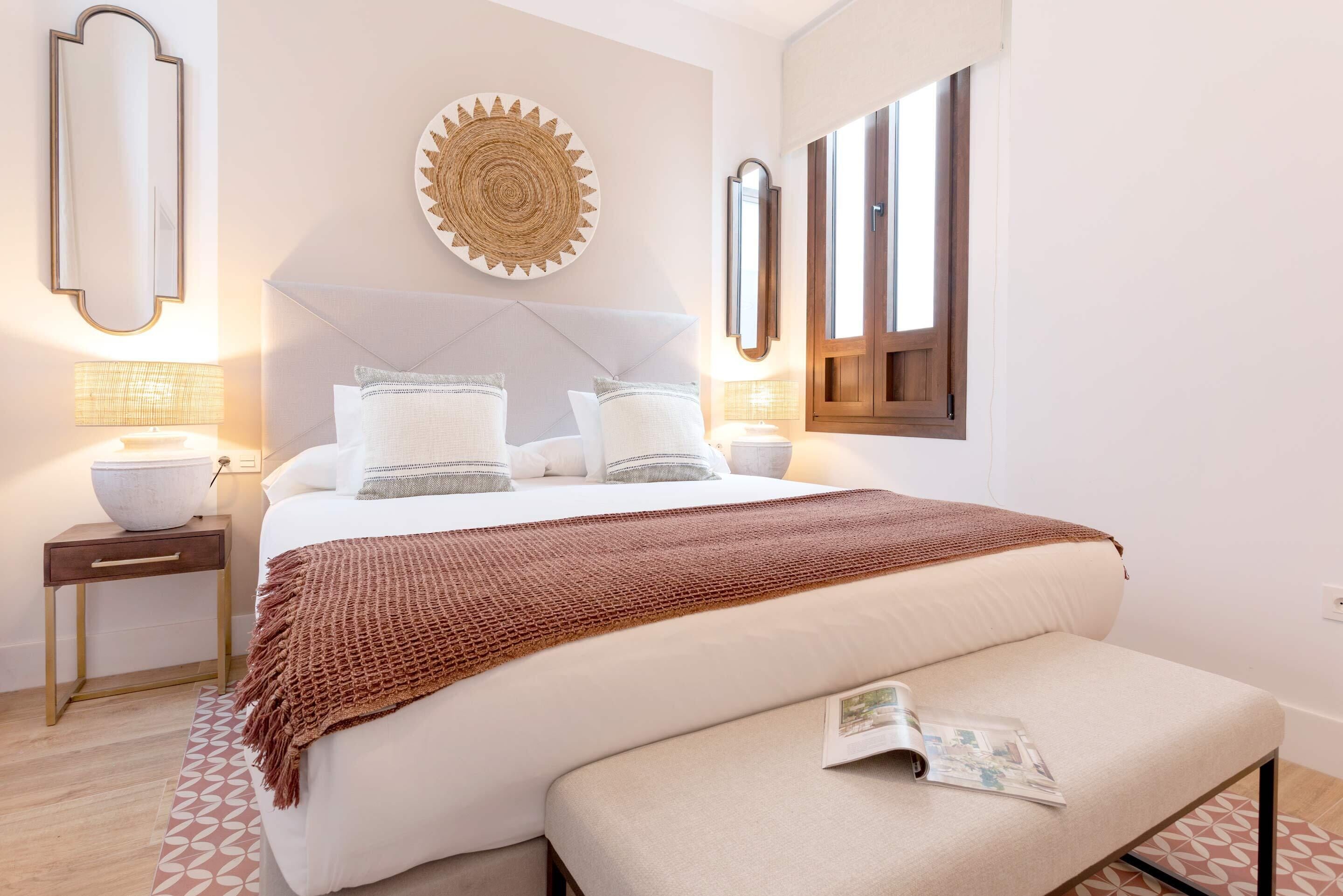 A neatly arranged bedroom with a large bed, bedside tables, a wall-mounted mirror, and a decorative plate.