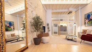 A modern living room with a large mirror, wooden flooring, a potted plant, a sofa, a red armchair, and a coffee table. - Genteel Home Santas Patronas (Seville)