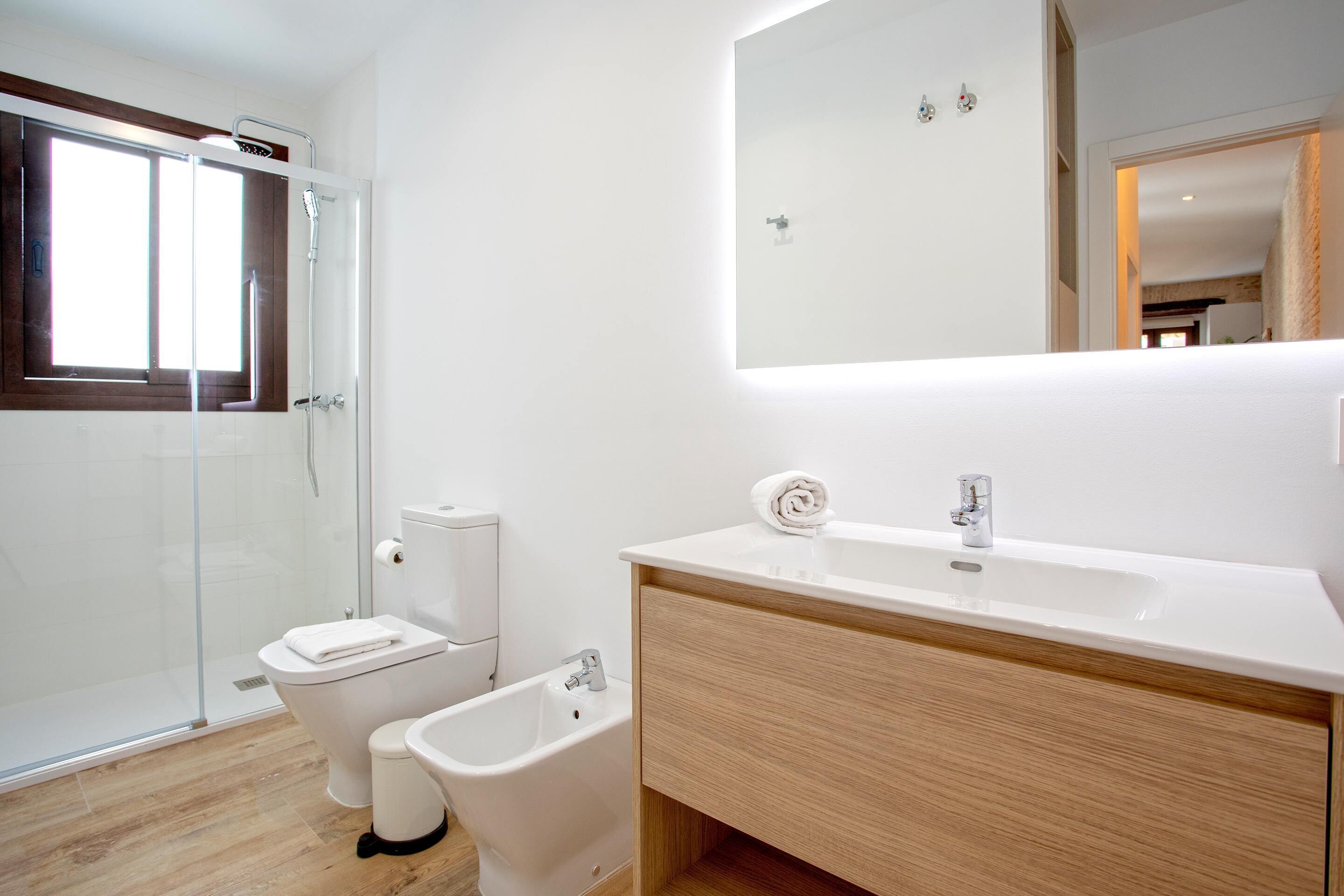 Une salle de bain moderne dotée d’une douche à parois de verre, de toilettes, d’un bidet et d’un meuble-lavabo avec un miroir.