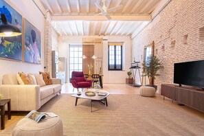 A spacious living room with a high ceiling, a large TV, a red armchair, and a sofa. - Genteel Home Santas Patronas (Seville)