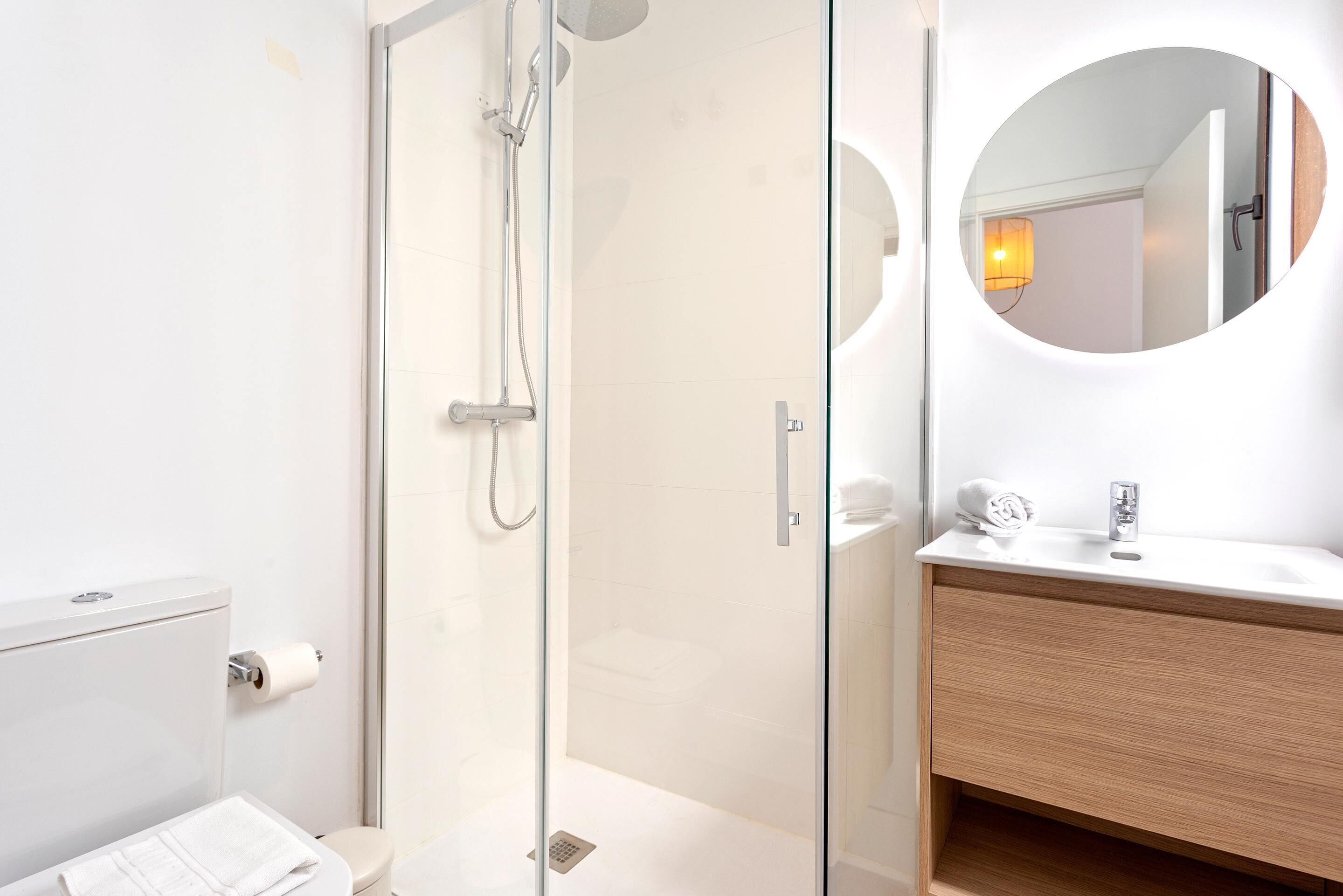 A modern bathroom with a glass-enclosed shower, a white toilet, and a wooden vanity with a mirror.