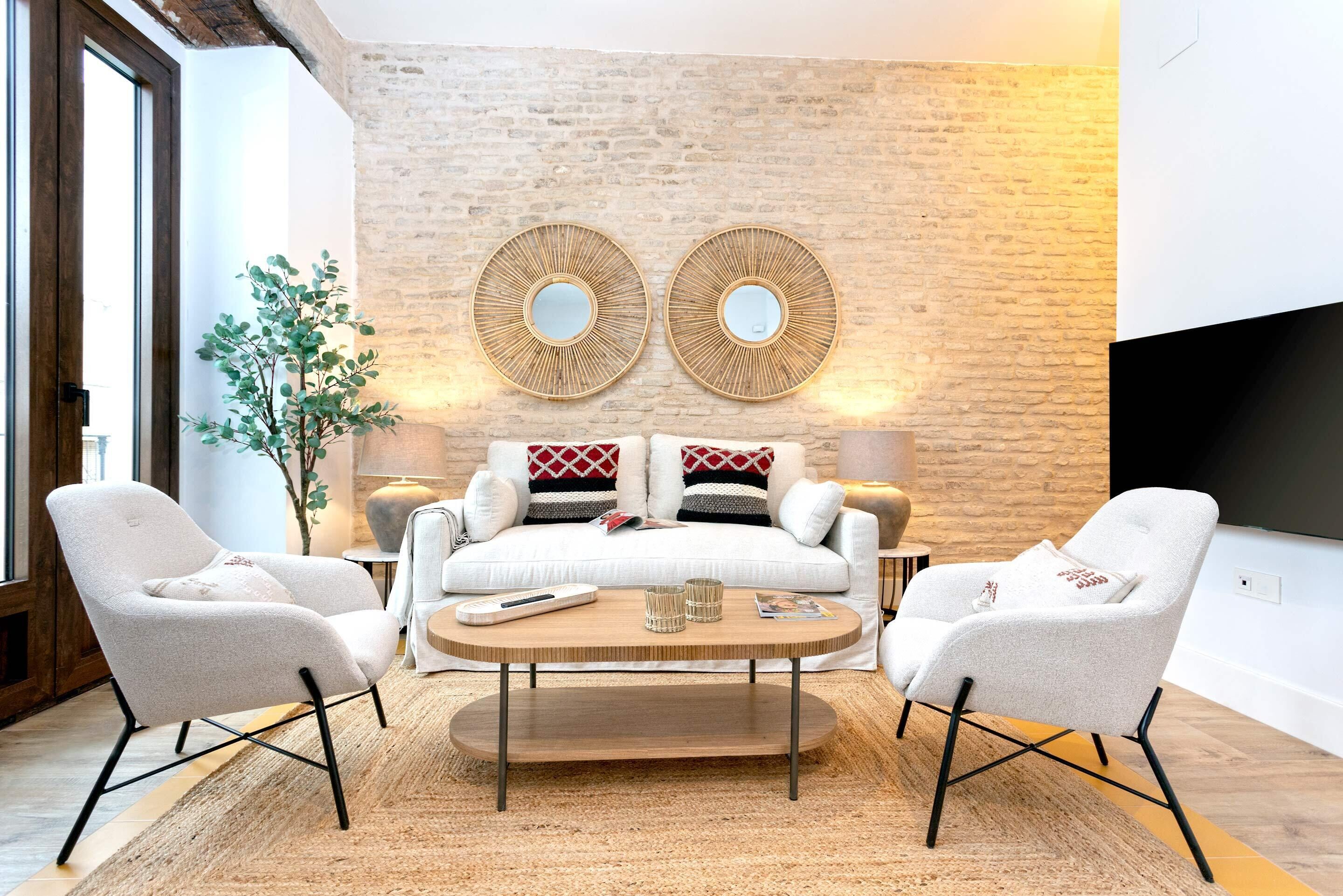 Een moderne woonkamer met een bank, twee fauteuils, een salontafel en decoratieve spiegels aan een bakstenen muur.