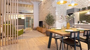 A dining area with a wooden table, chairs, and a brick wall. There is a plant on the table and a kitchen area in the background. - Genteel Home Santas Patronas (Seville)