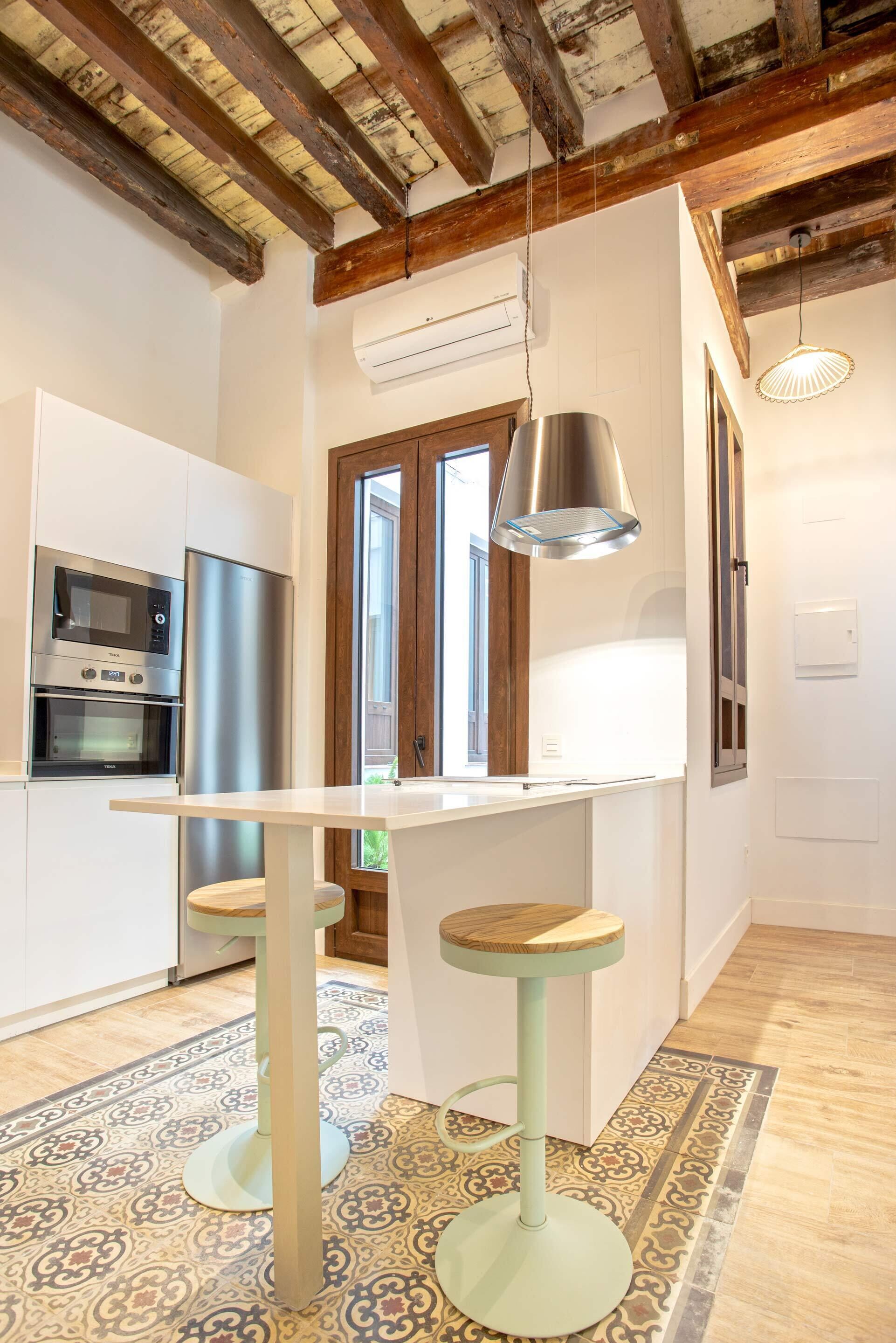 Une cuisine moderne dotée d’appareils électroménagers en acier inoxydable, d’un plafond en bois et d’un tapis à motifs.