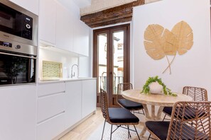 A modern kitchen with white cabinets, a stainless steel oven, and a dining area with wicker chairs and a wooden table. - Genteel Home Santas Patronas (Seville)
