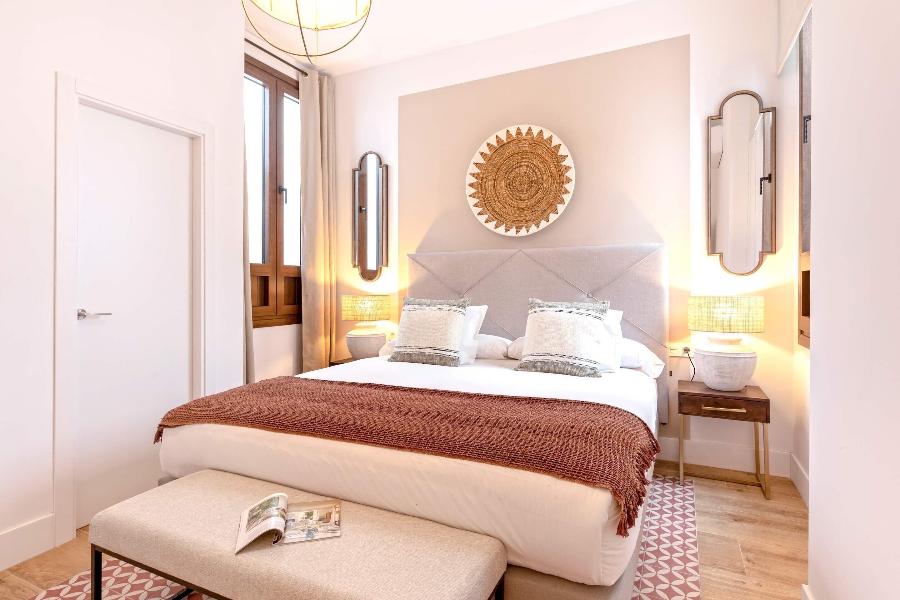 Une chambre à coucher moderne avec un grand lit, une table de chevet, un banc pour lire et un miroir fixé au mur.