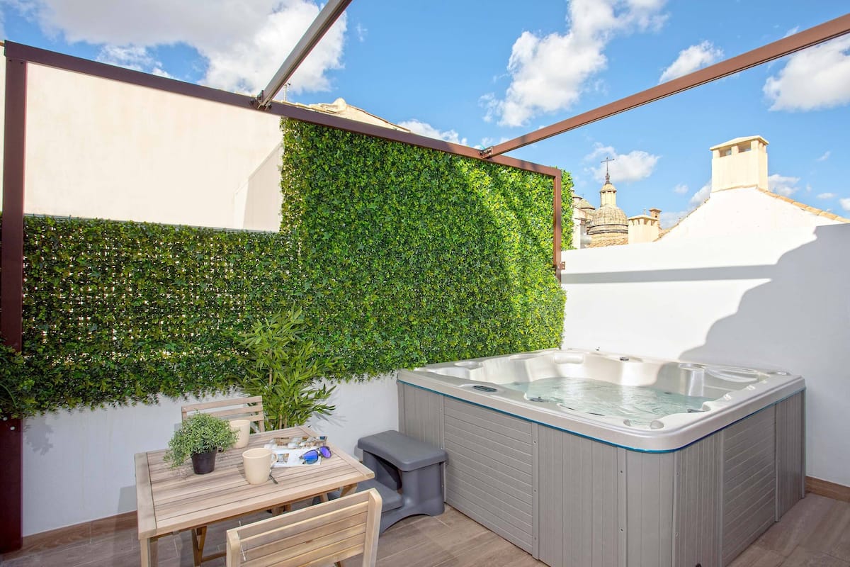 A rooftop patio with a hot tub, a wooden table, and a green wall.