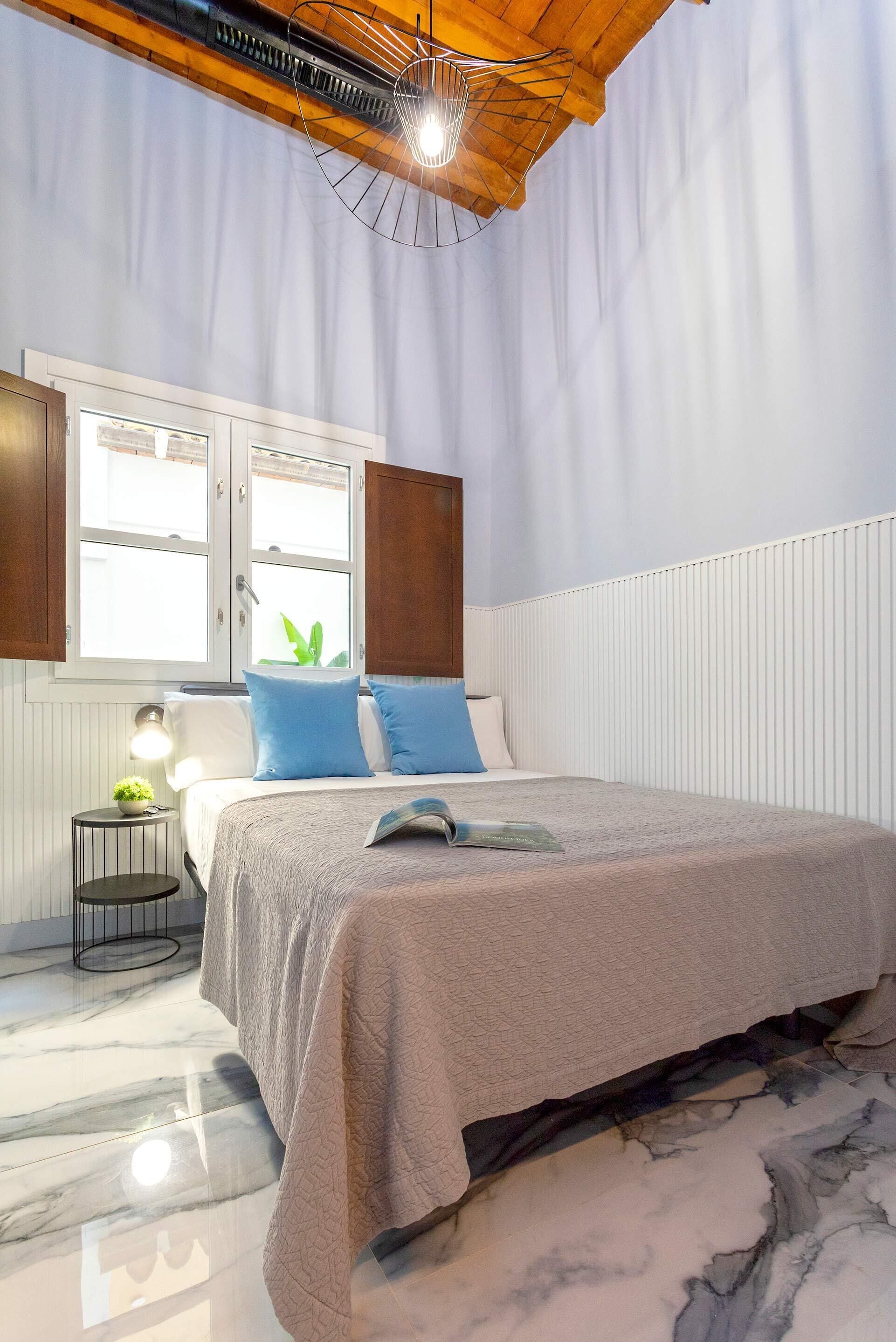A bedroom with a bed, a window, a bedside table with a lamp, and a radiator.