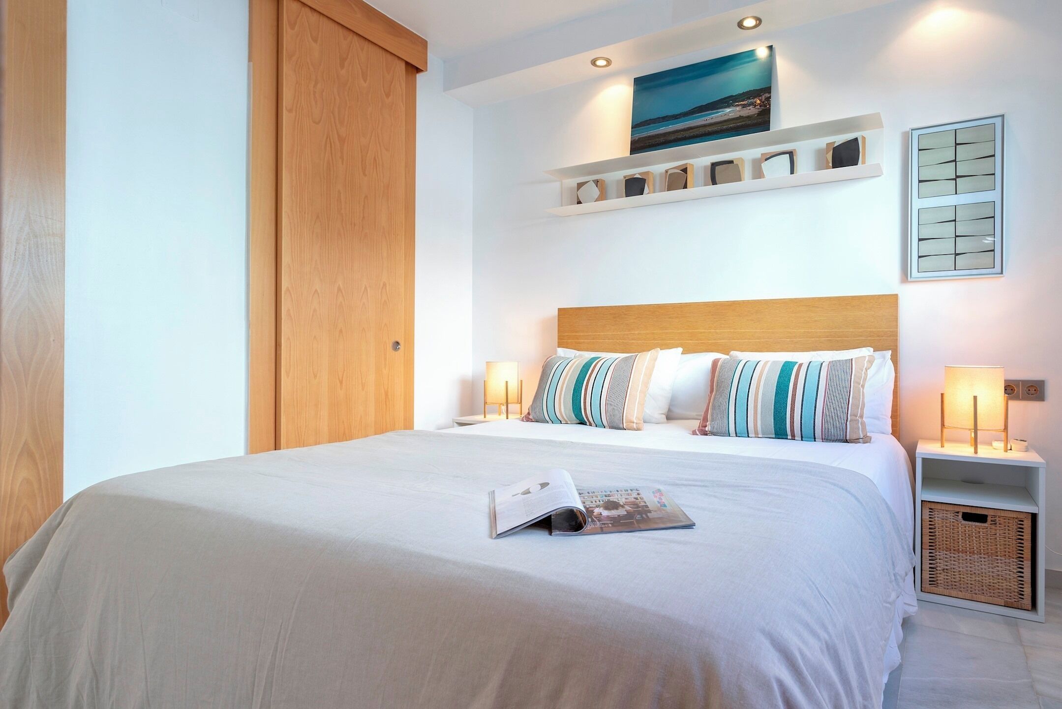 A neatly made bed with a magazine, a wooden headboard, and bedside lamps.