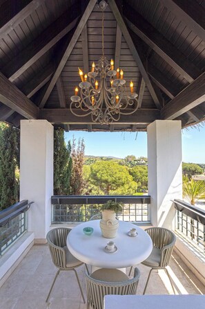 A covered outdoor seating area with a table and chairs, a chandelier, and a view of a green landscape. - Genteel Home Incosol (Marbella)