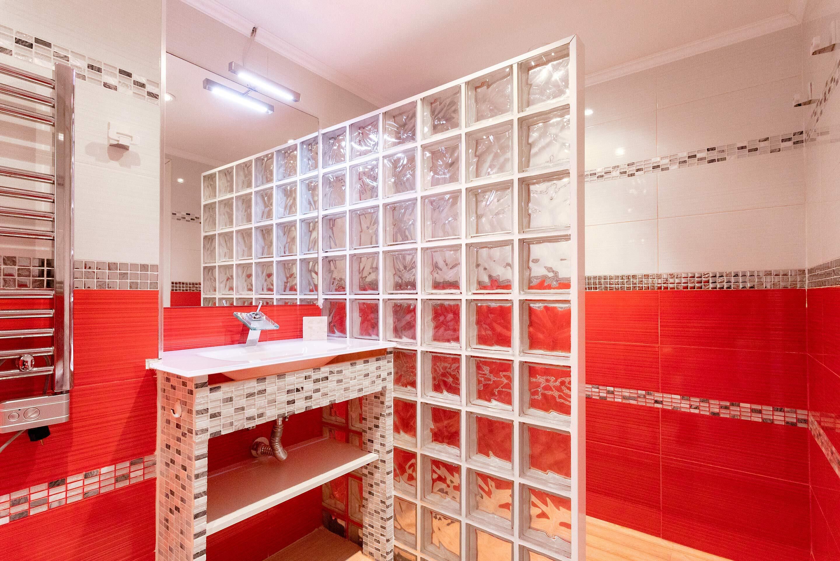 A bathroom with a red and white tiled wall, a white sink, and a mirror.