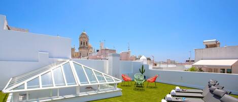 Una terrazza sul tetto con una serra in vetro, sedie verdi, poltroncine relax e un cactus.