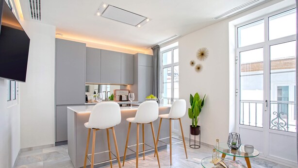 Una cucina moderna con isola centrale, sgabelli da bar e un tavolo in vetro con una rivista.