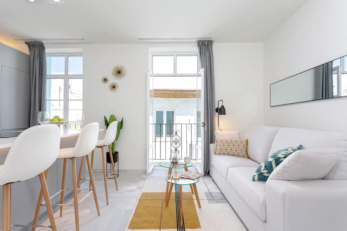 Un salon moderne avec un canapé blanc, une table basse en verre et un coin repas comprenant des chaises blanches et une table en verre.