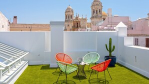 Una terrazza sul tetto con tavolo e sedie, un cactus in vaso e vista su edifici storici.