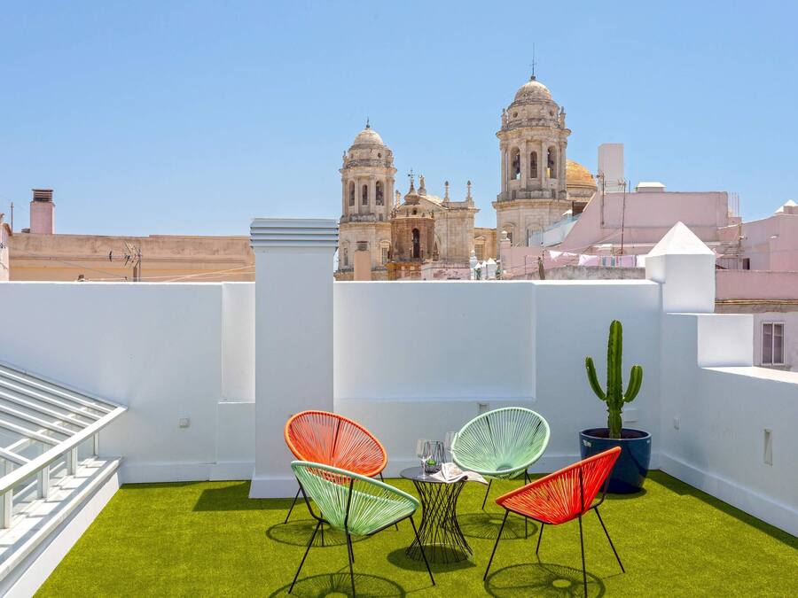 Terraço no telhado com mesa e cadeiras, um cacto em vaso e vista de edifícios históricos.