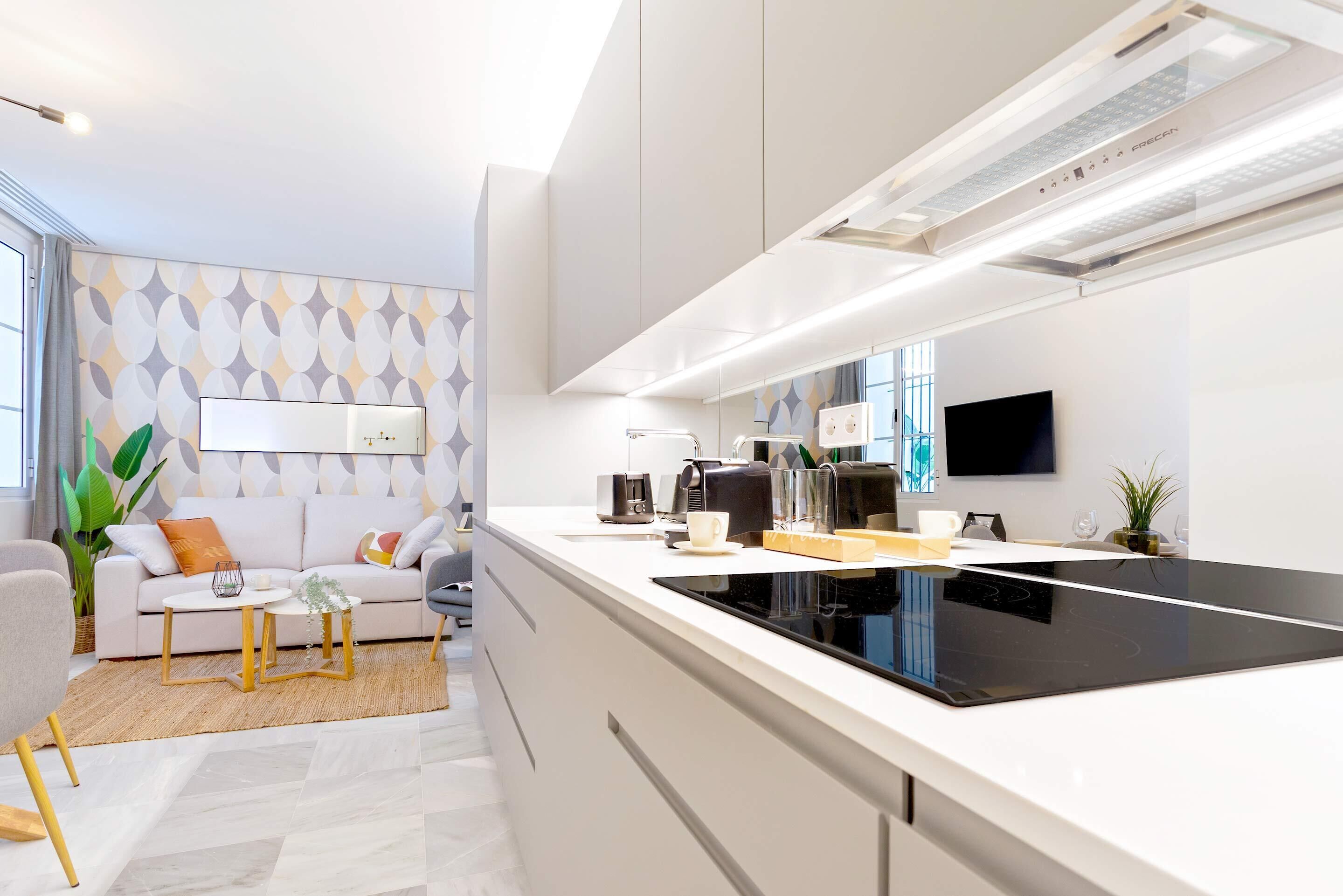 A modern kitchen with a black stovetop, white cabinets, and a built-in oven. There is a dining area with a white table and chairs, and a large window providing natural light.
