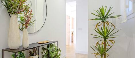 A hallway with a console table holding potted plants and a large mirror.