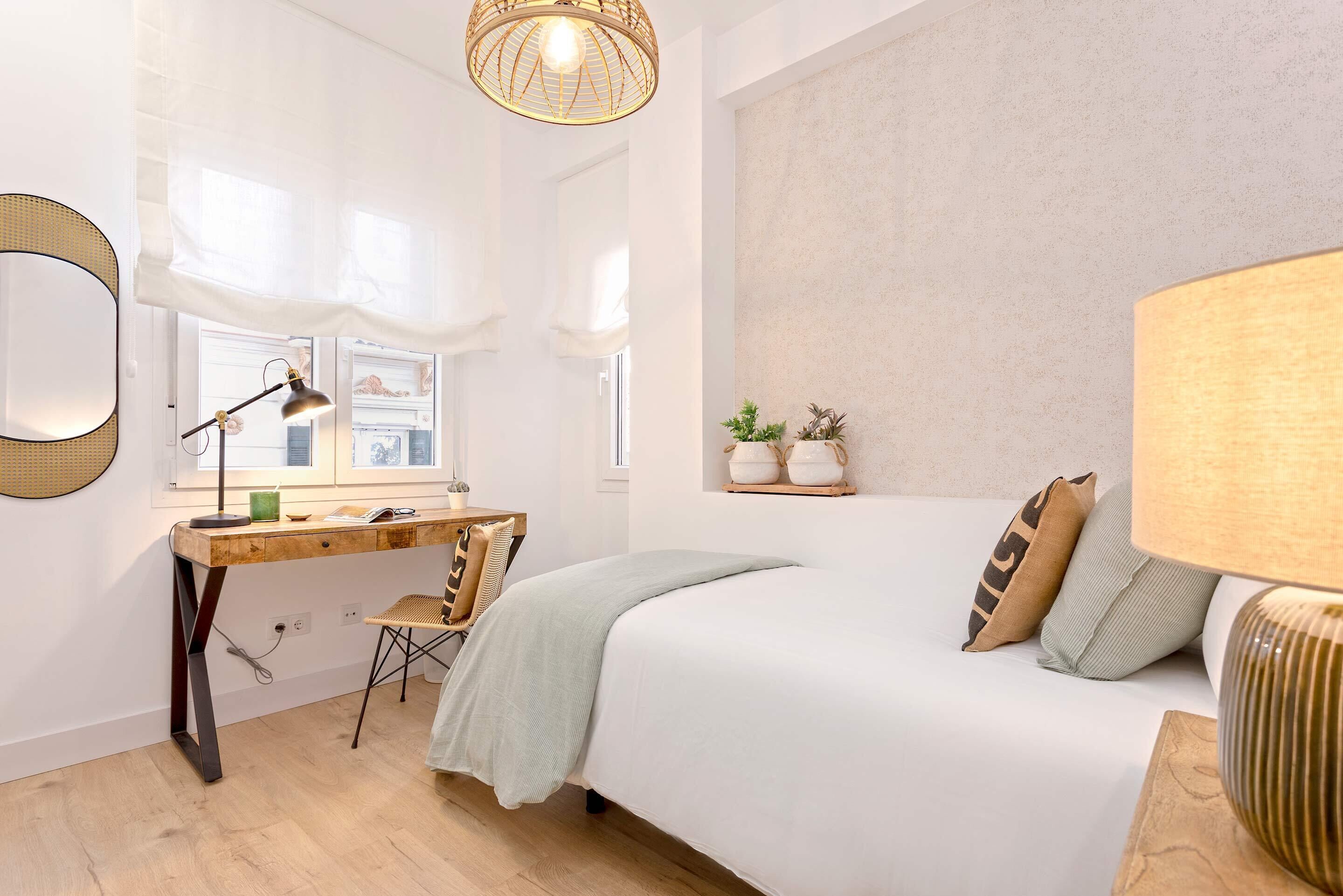 A bedroom with a bed, a desk, a chair, a lamp, and a window with curtains.