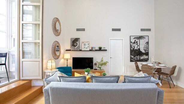 A modern living room with a grey sofa, a TV, and a dining area with wicker chairs. - Genteel Home San Agustín (Málaga)