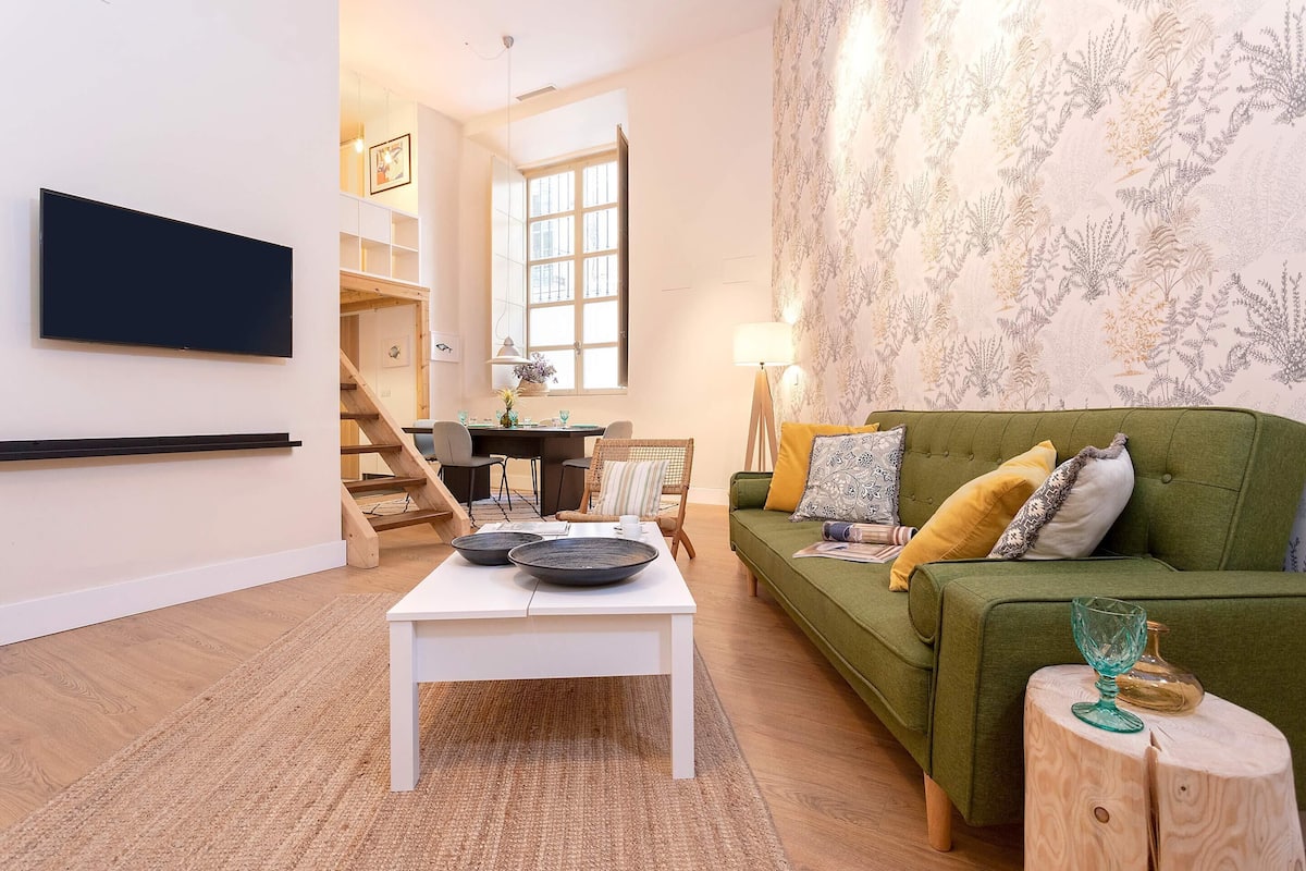 A living room with a green sofa, white coffee table, and a flat-screen TV mounted on the wall.