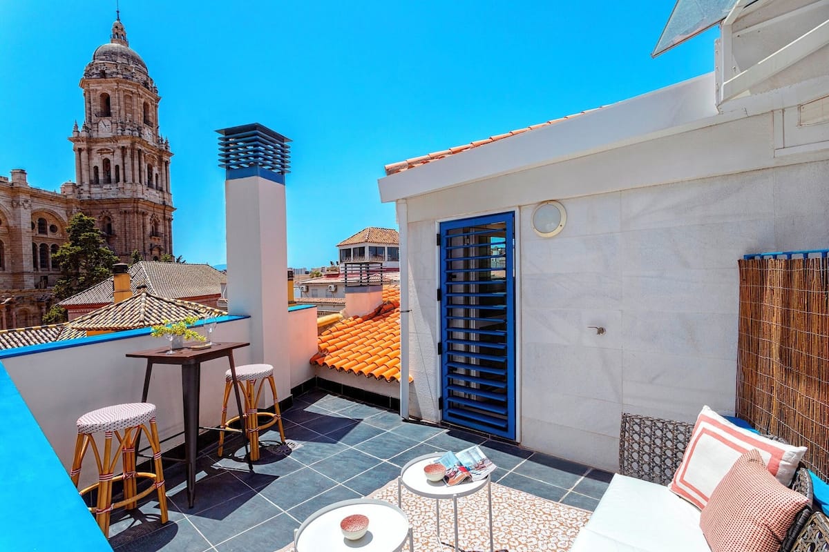 A rooftop terrace with a view of a historic building, a blue door, and a small table with stools.
