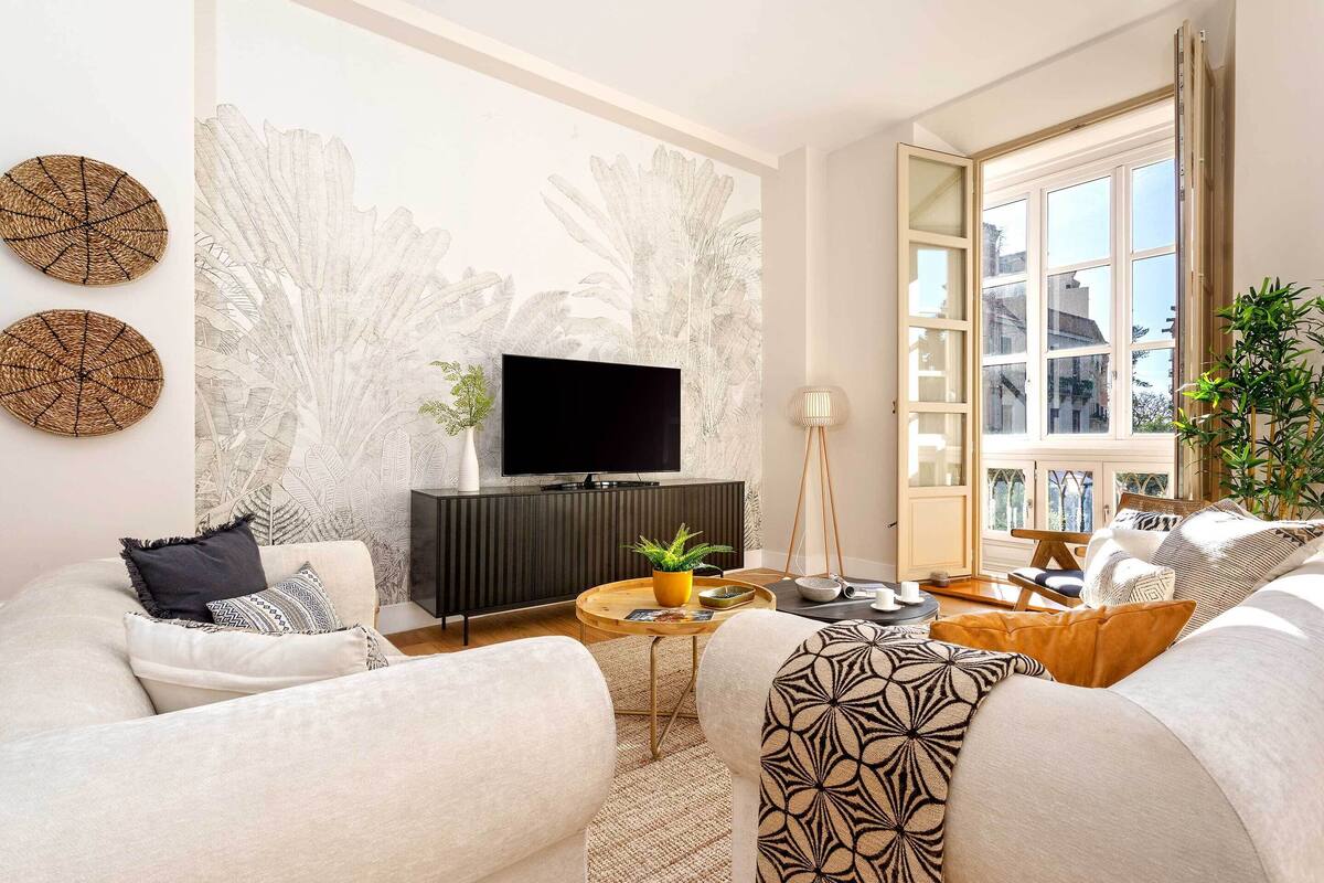 A modern living room with a flat-screen TV, a sofa set, a coffee table, and a large window with a view.