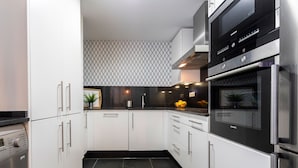 A modern kitchen with white cabinets, a black countertop, and stainless steel appliances including a microwave and oven. - Genteel Home San Agustín (Málaga)
