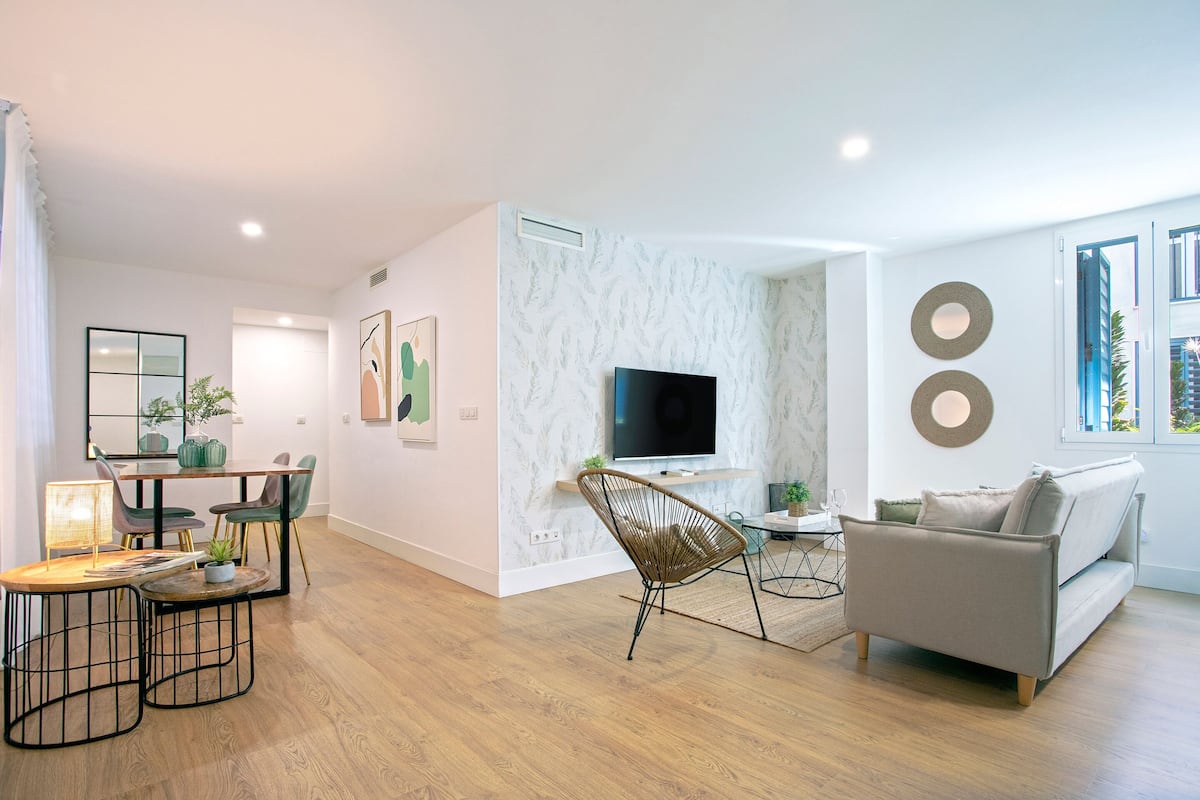 A modern living room with a dining area, a sofa, a TV, and a large window.