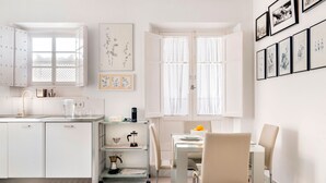 Une cuisine moderne avec des meubles blancs, un coin repas comprenant une table et des chaises, et des œuvres d’art accrochées aux murs.
