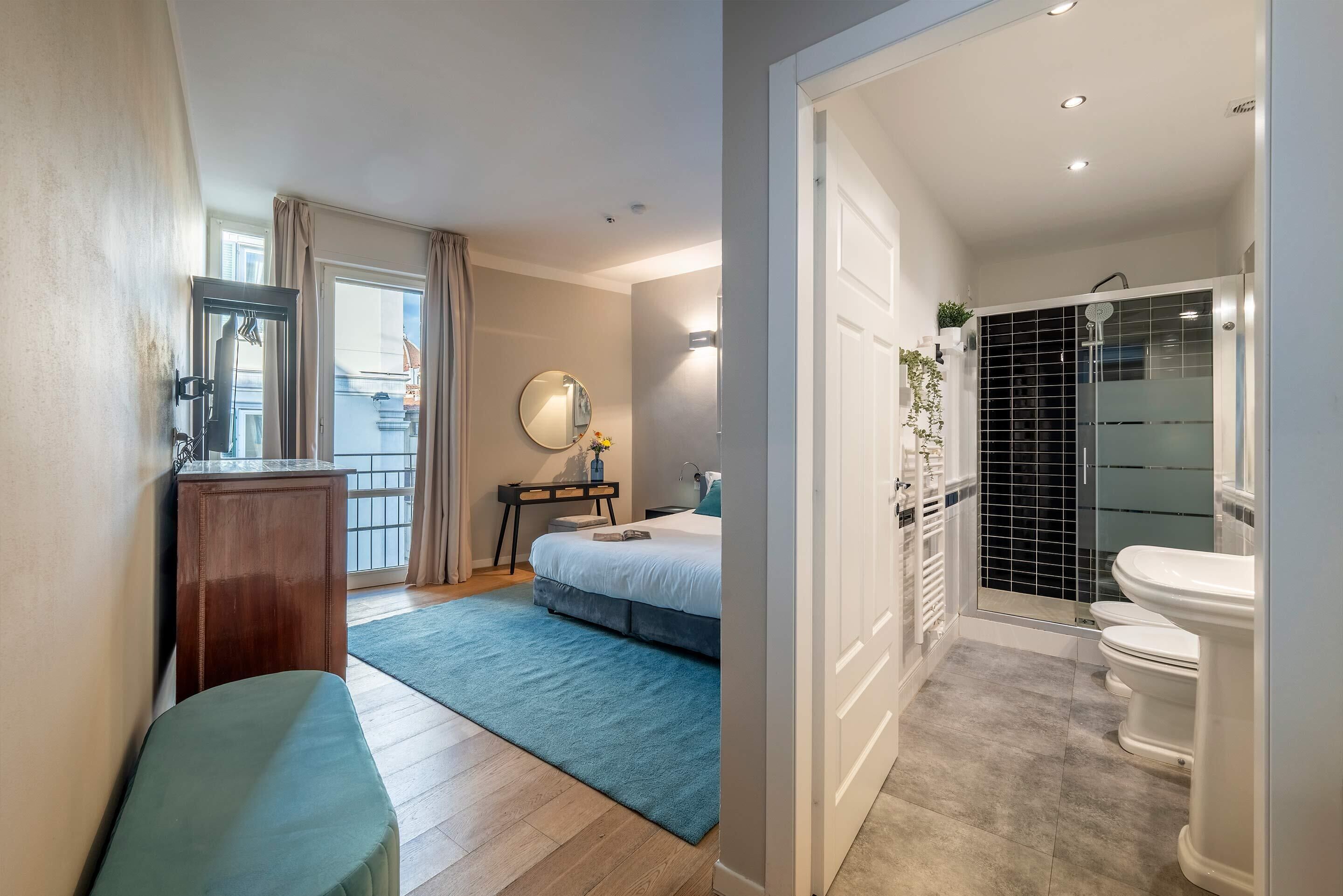 Un dormitorio con cama, mesita de noche y vistas al exterior. El baño tiene inodoro, lavabo y ducha.