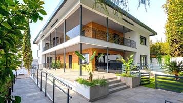 A modern two-story building with large windows, a balcony, and a paved entrance area with planters.