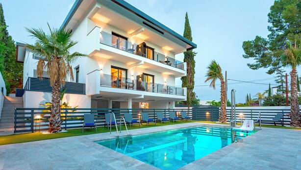 A modern two-story house with a swimming pool, outdoor seating, and palm trees.
