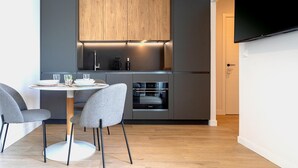 A modern kitchen with grey cabinetry, a built-in oven, and a dining area with a round table and grey chairs.
