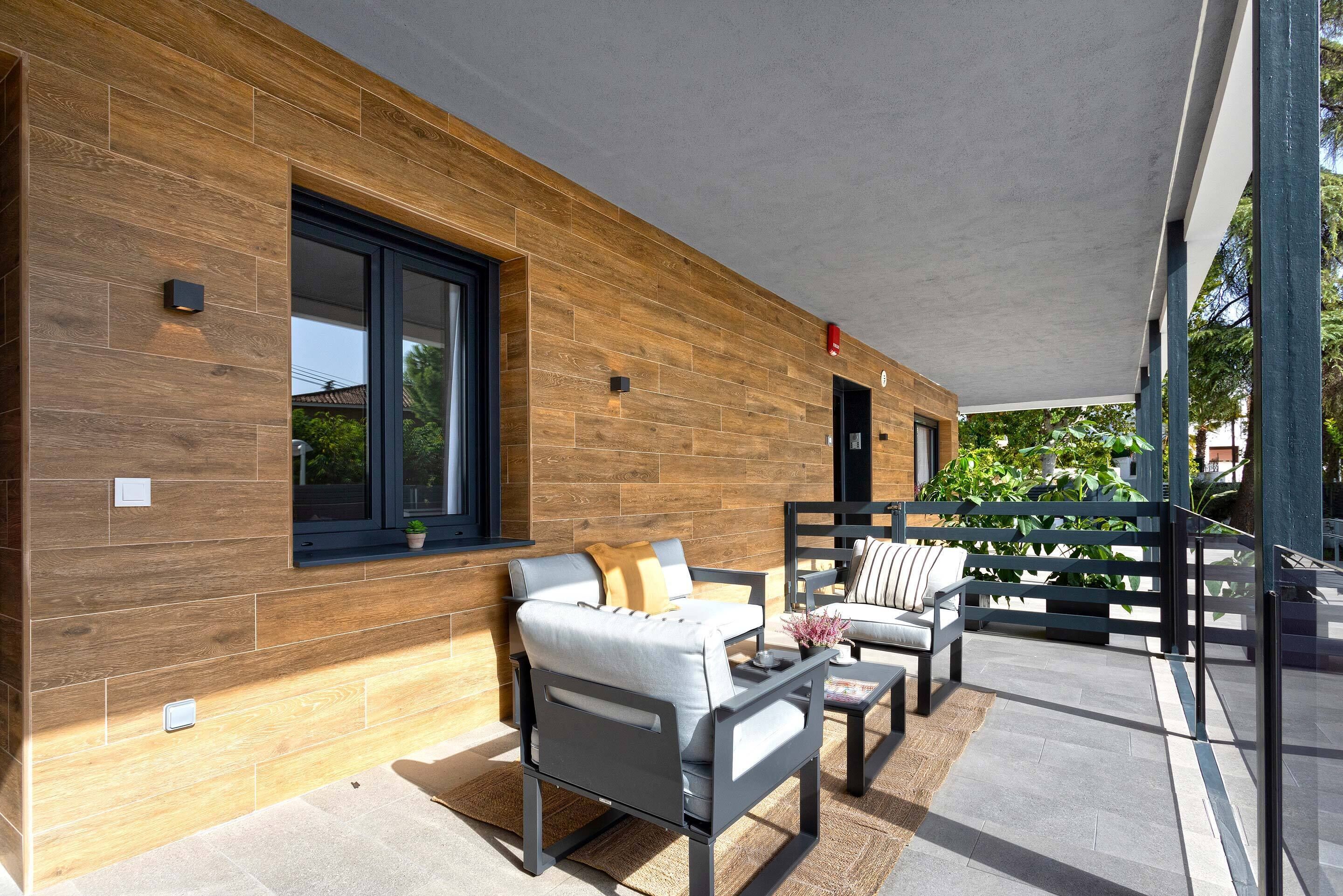 An outdoor seating area with modern furniture, a wooden wall, and a covered patio.