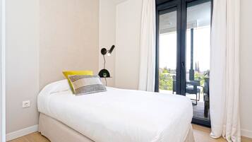 Une chambre à coucher comprenant un lit, une table de chevet, une lampe et une vue sur l’extérieur grâce à une porte coulissante.