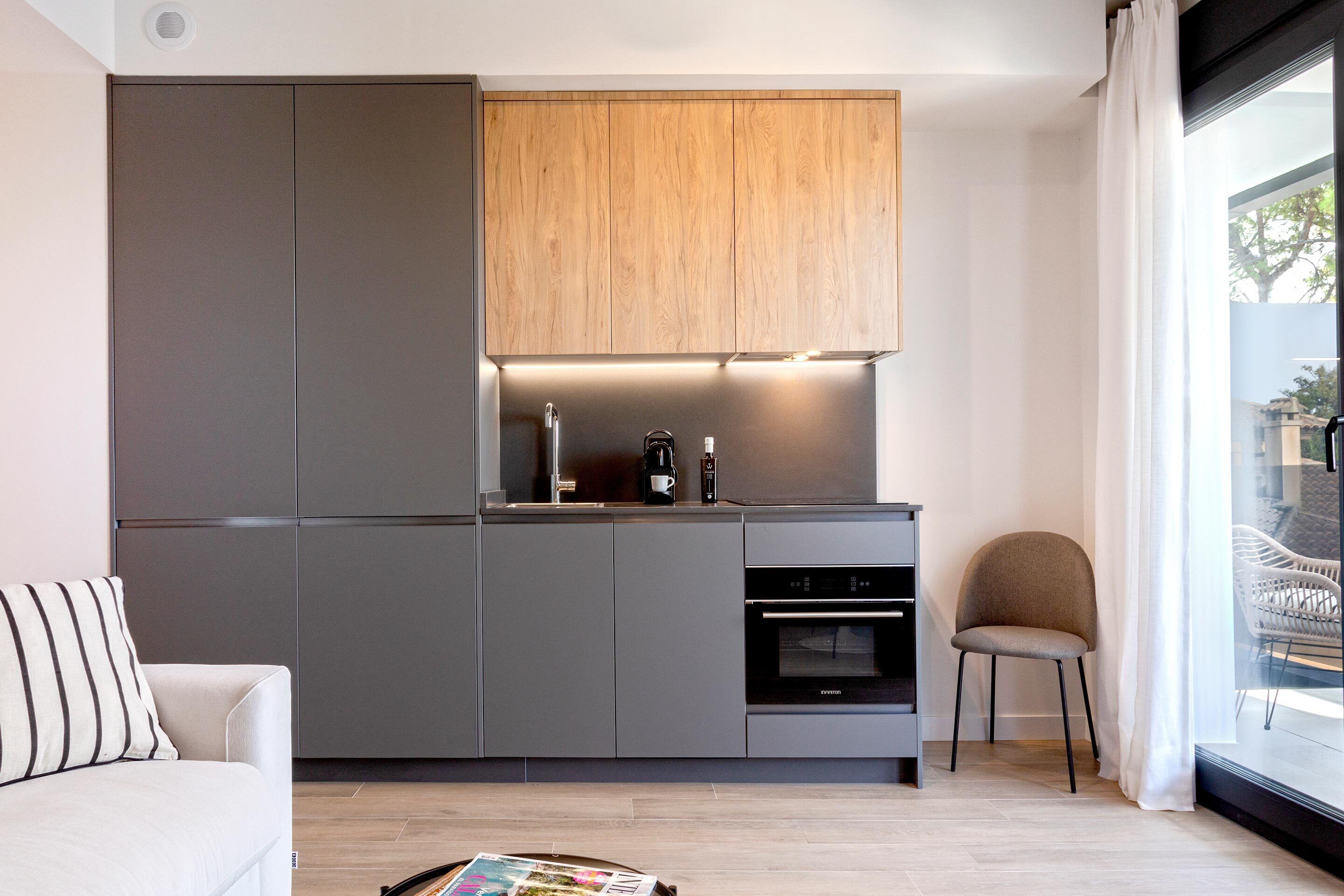 A modern kitchen with grey cabinets, a wooden upper section, a built-in oven, and a window with a view of the outside.